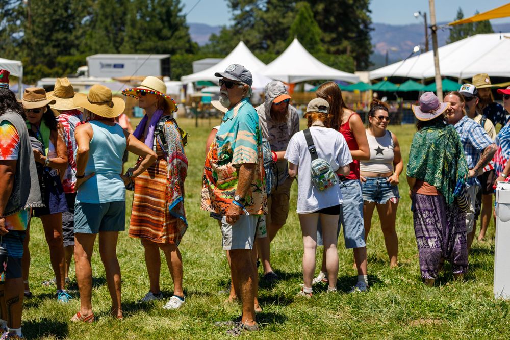 Festival attendees in sunhats gathering at outdoor summer market with white tents.