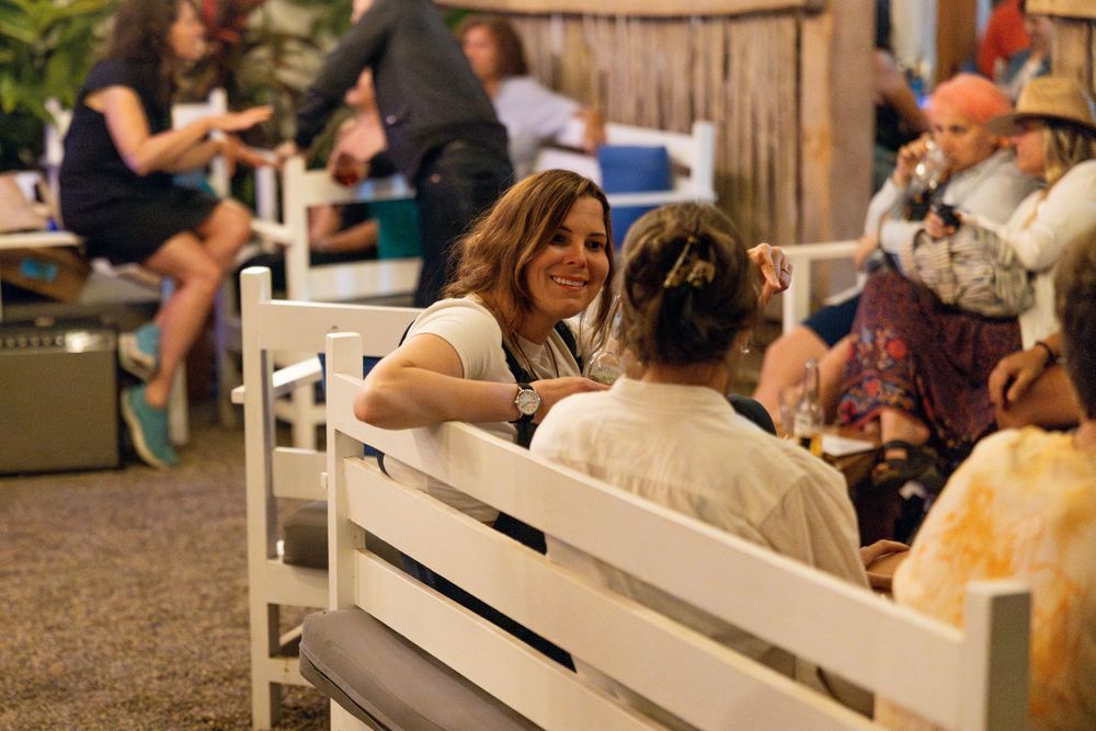 Casual outdoor dining area with people seated on white benches in warm lighting.