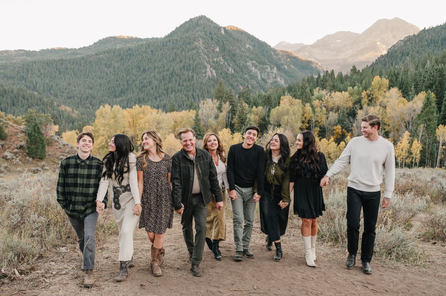 A group walks together along a mountain trail during autumn with scenic peaks in the background.