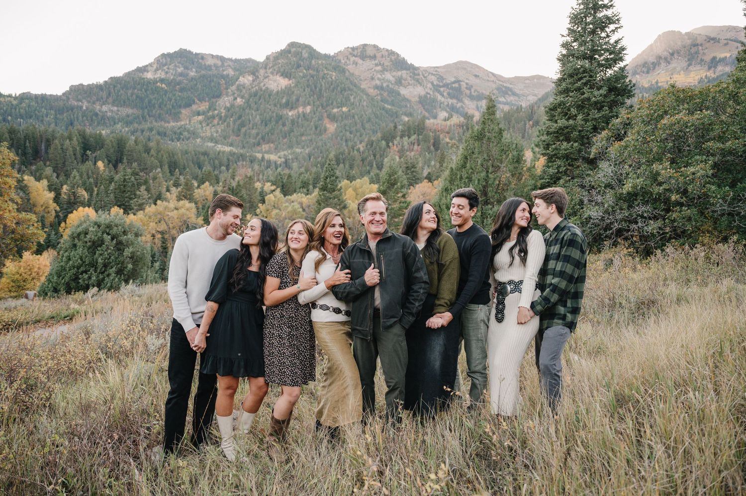 Friends gather for a group photo on a mountainside with fall foliage and peaks in the background.