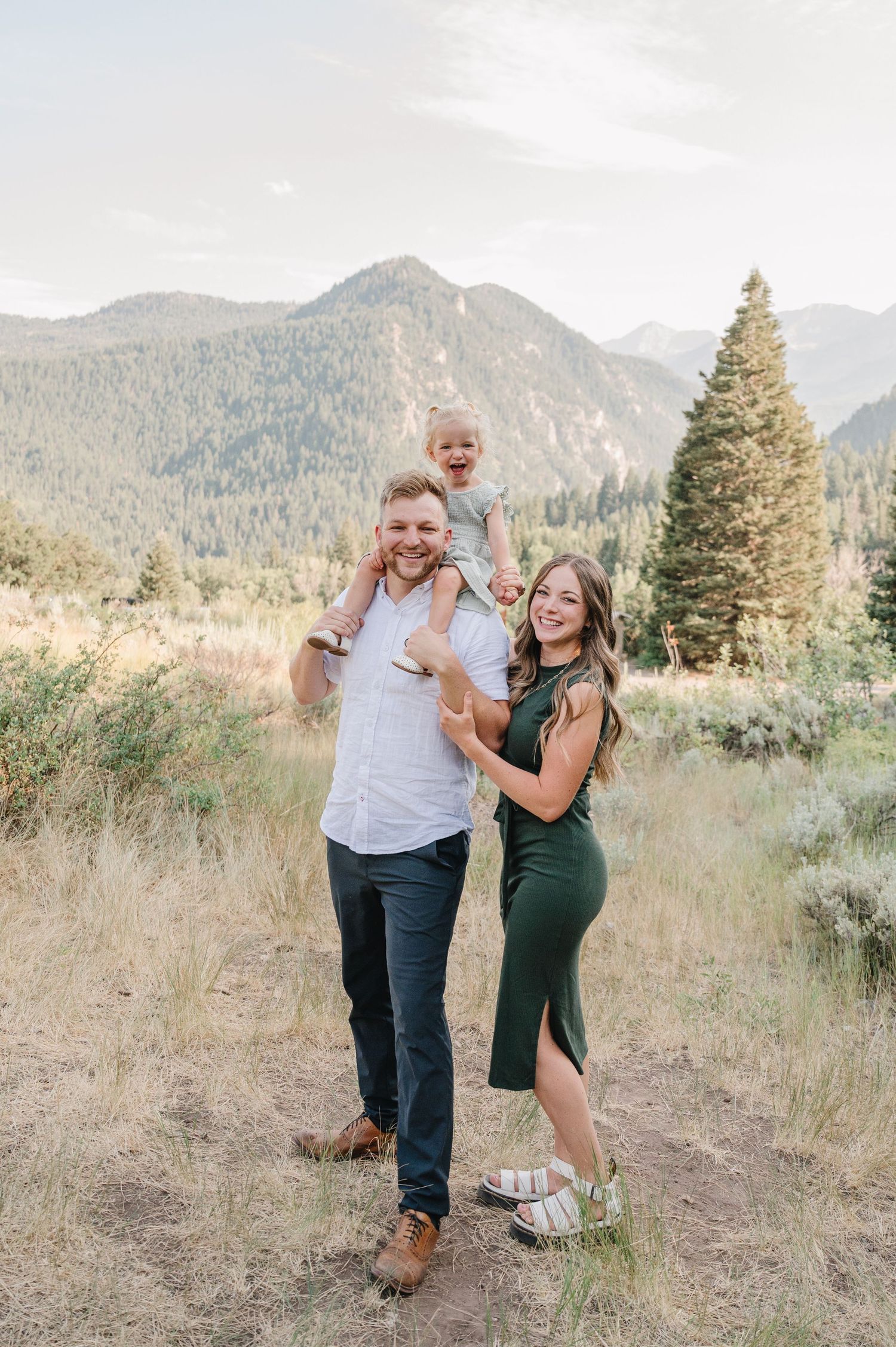 Joyful outdoor family photo session in a mountain valley with golden grass and evergreens.