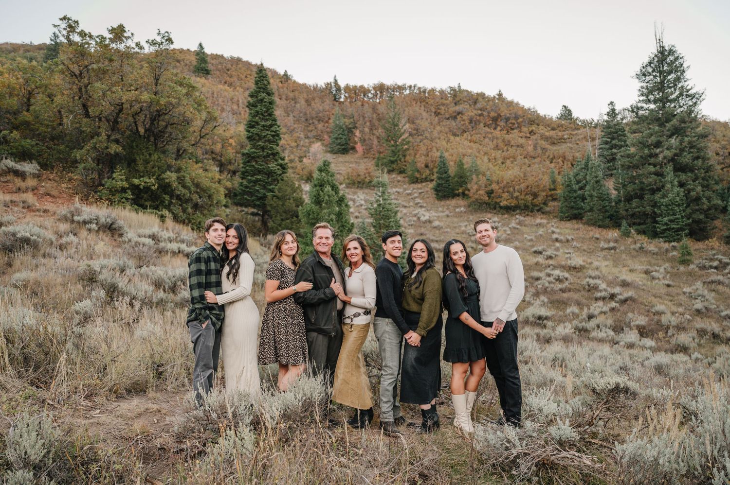 Group photo of people standing on a hillside with mountains and autumn vegetation in the background.