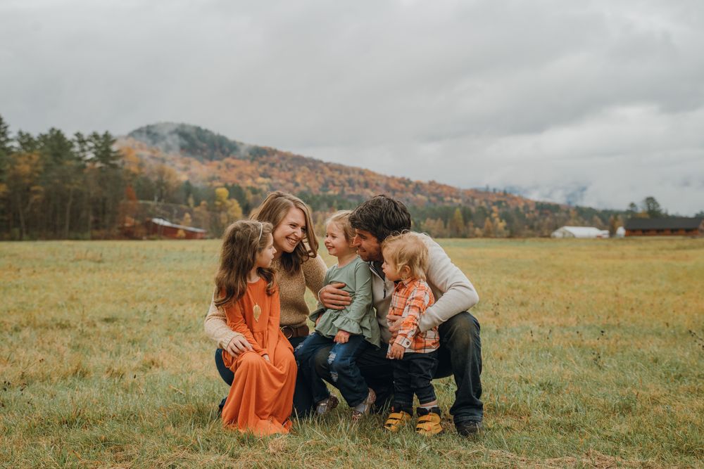 Happy family with three young children shares a joyful embrace in an autumn field with mountain views.