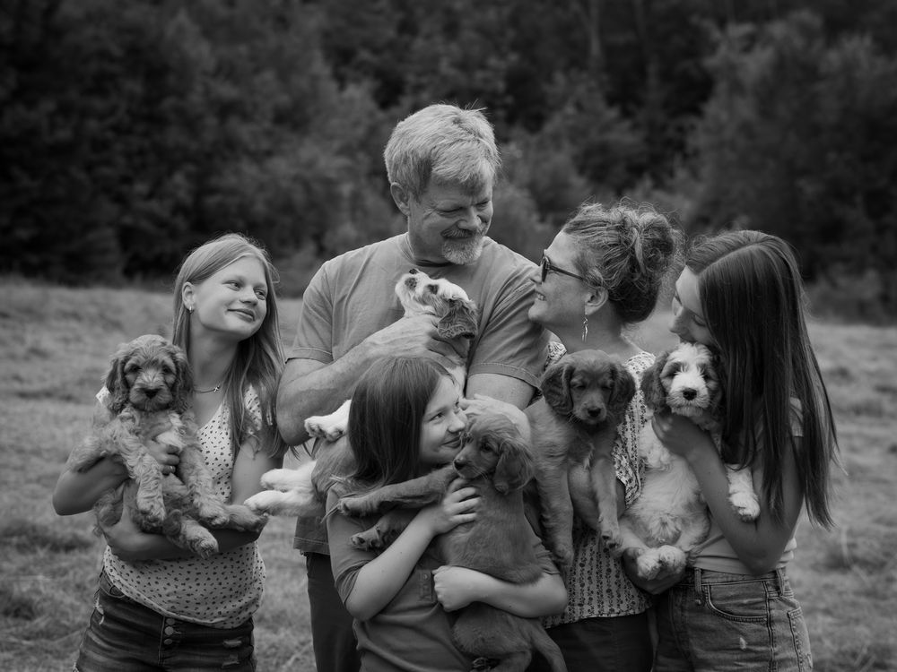 Family laughs together while holding playful puppies in a black and white outdoor portrait.