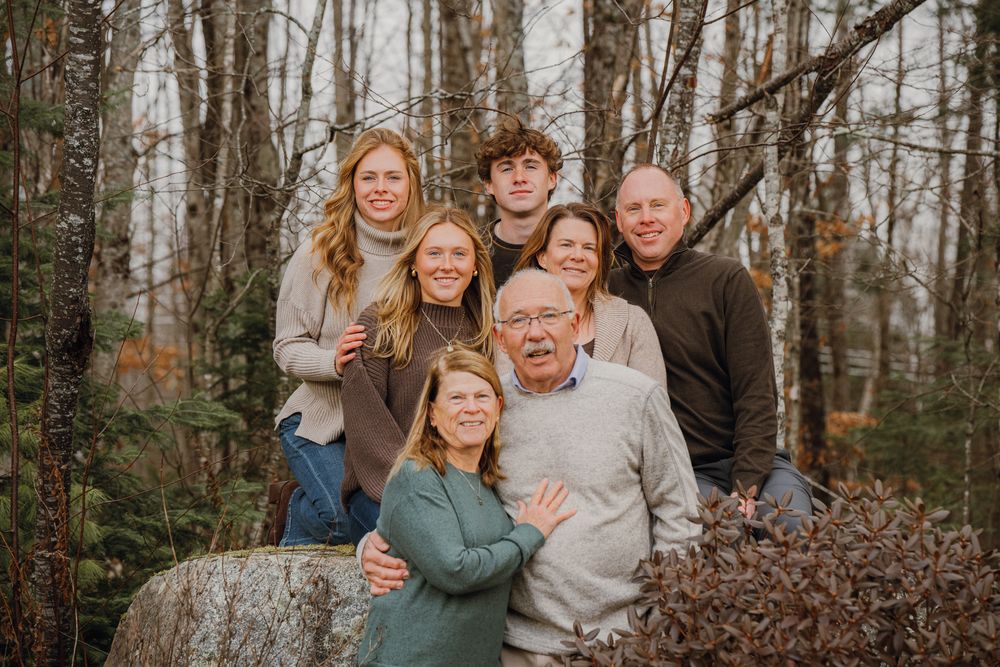 Family of seven posing outdoors among trees on rocks for a fall portrait photo session.