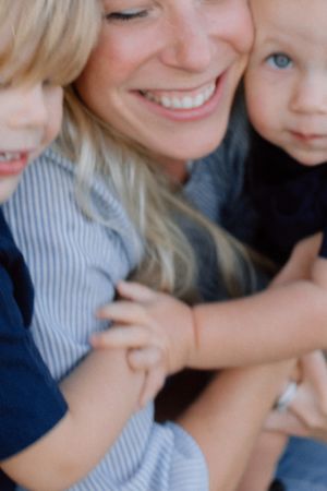 Joyful mother with bright smile cuddling two young blonde children in a warm close-up portrait.