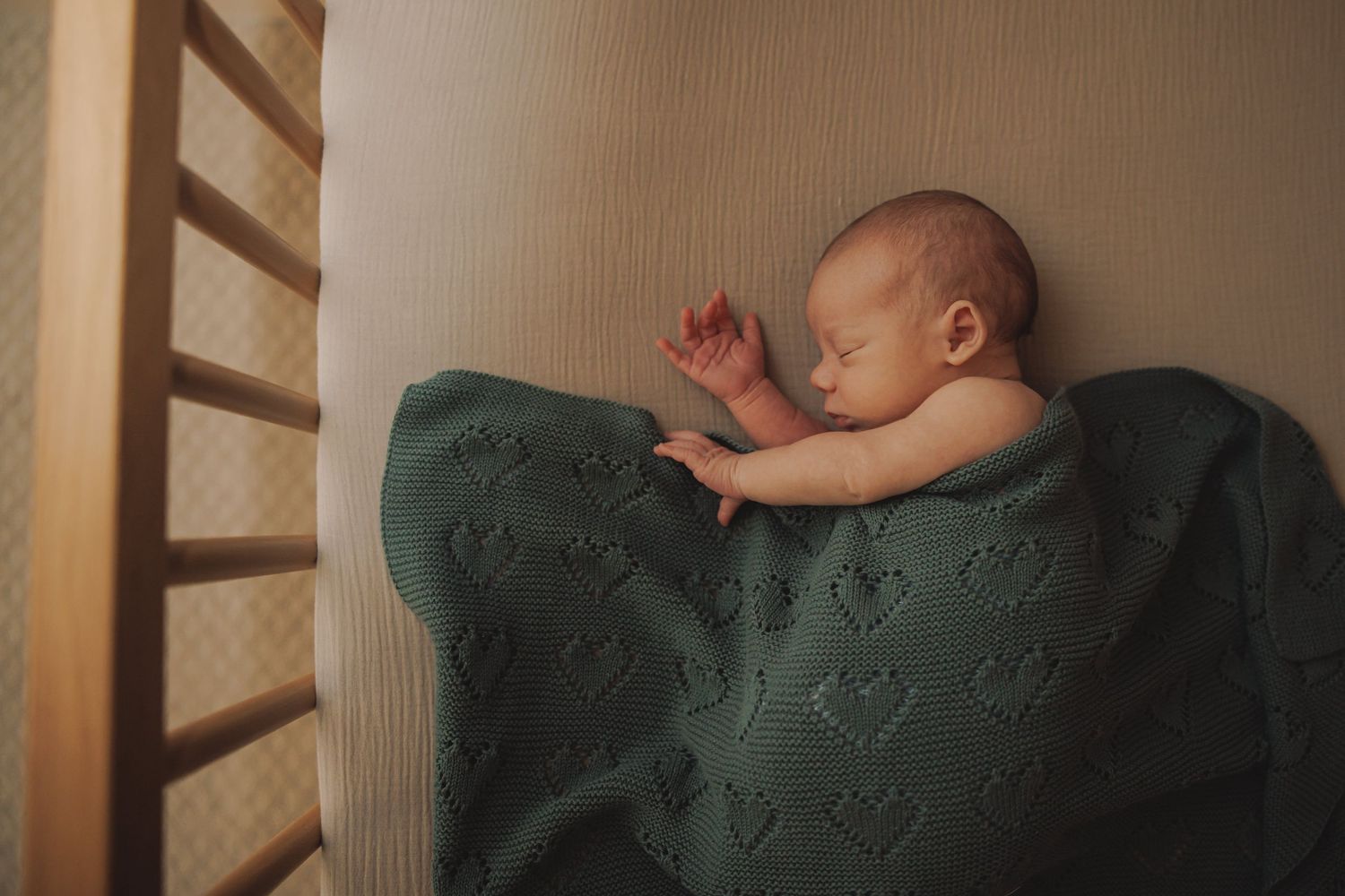 Sleeping baby wrapped in a soft mint green knitted blanket on white bedding.