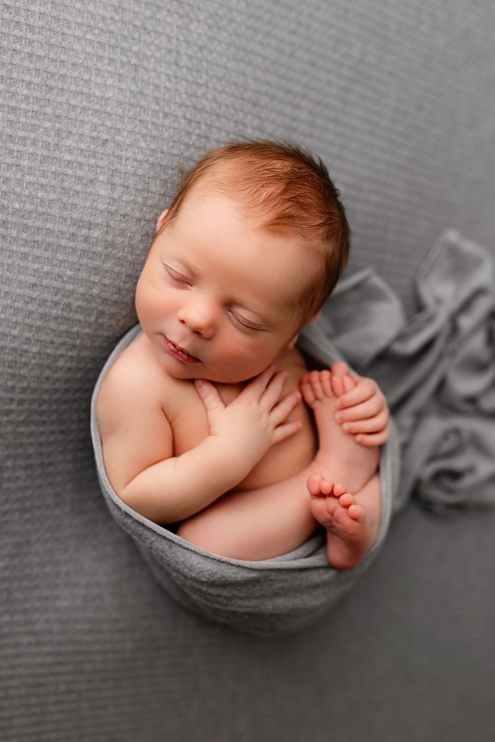 Sleeping newborn baby in gray bowl pose with knit wrap at professional photography studio in Summerville SC