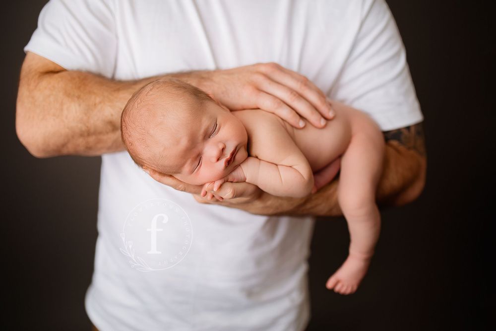Newborn baby cradled safely in father's protective hands during studio portrait session in Summerville SC