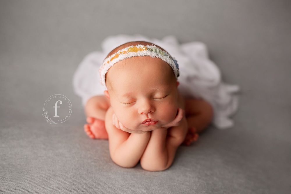 Newborn baby in froggy pose wearing delicate floral headband at Flowertown Photography studio in Summerville SC