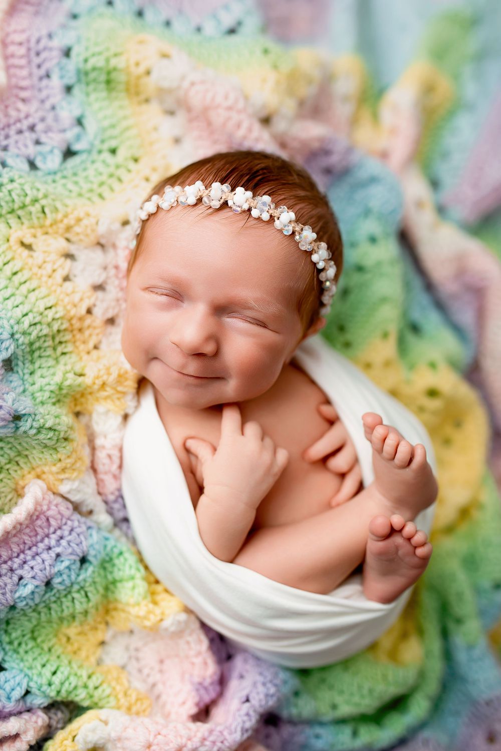 Smiling newborn baby girl with pearl headband on colorful rainbow blanket at Summerville SC photography studio