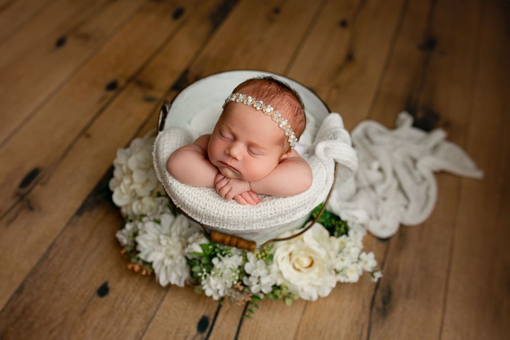 Newborn baby girl sleeping in white bucket with pearl headband and white flowers by Summerville SC photographer