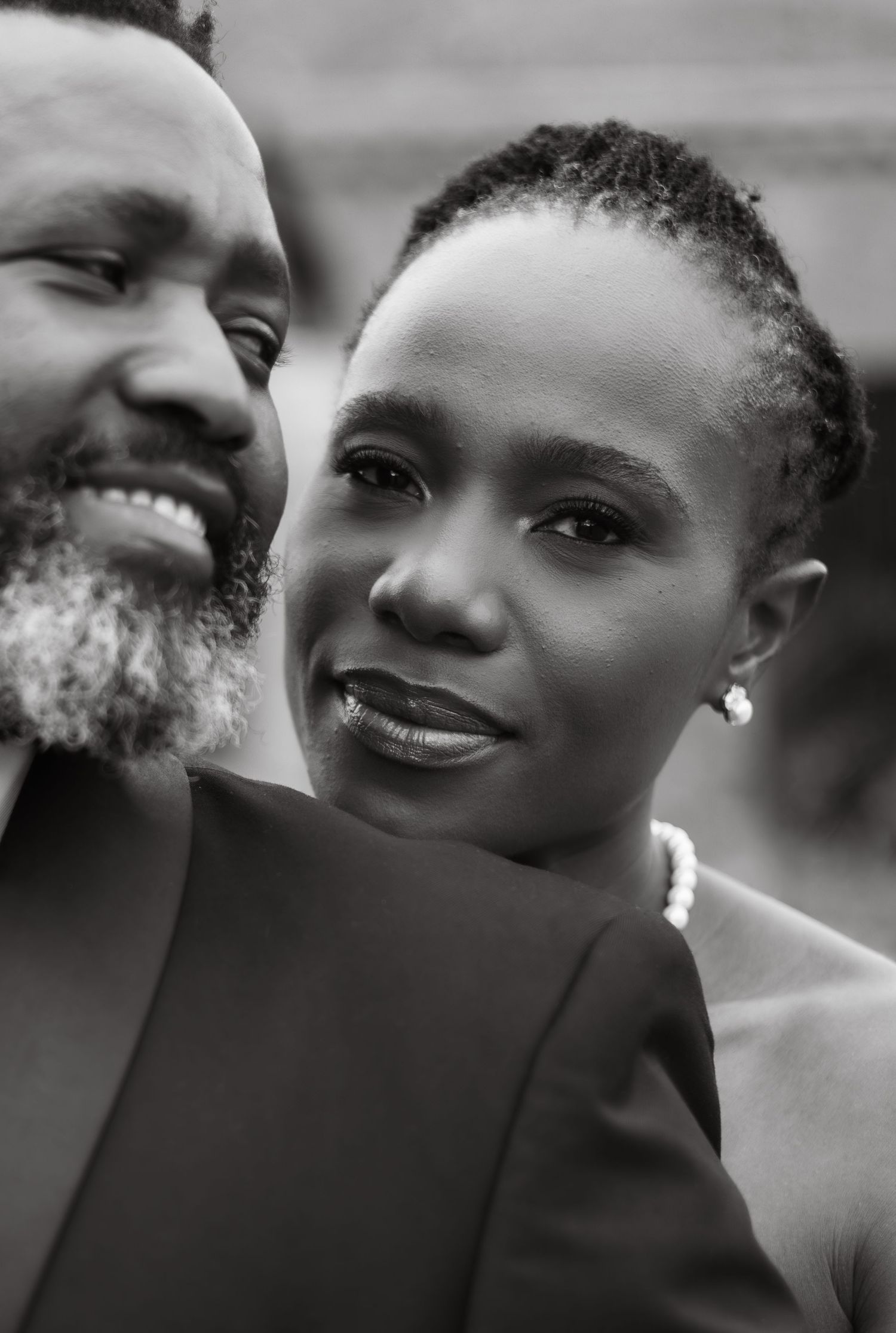 A close-up black and white portrait of a couple wearing elegant attire and smiling warmly at the camera.