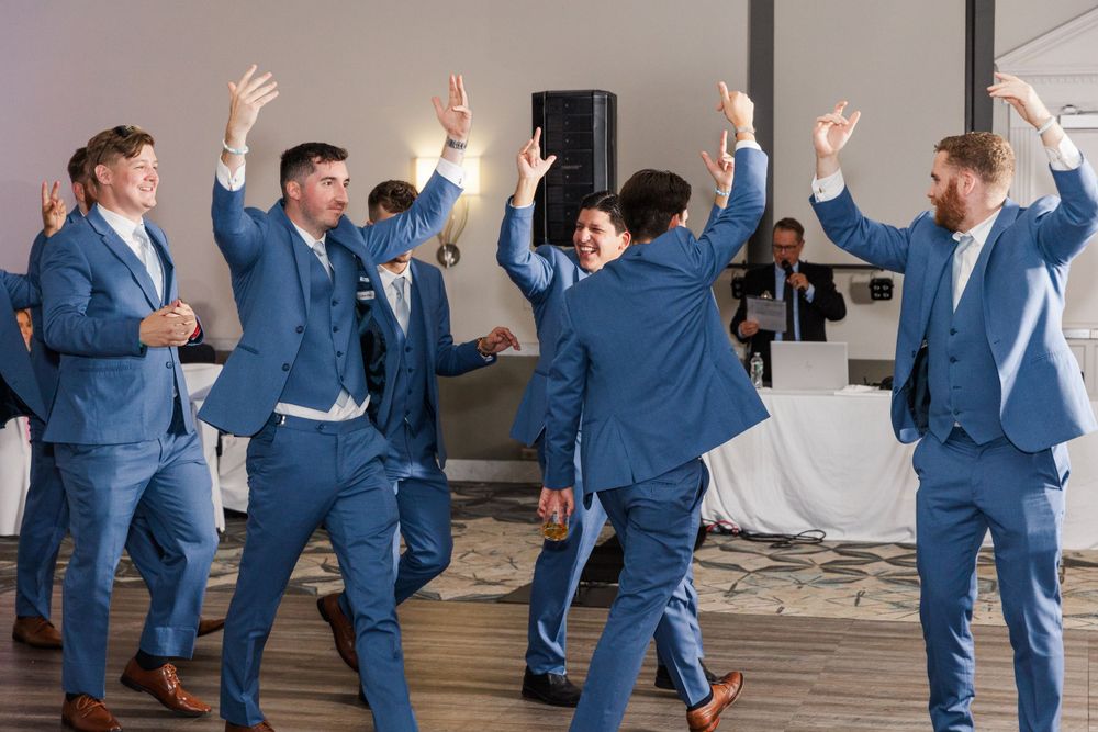 Group in matching blue suits dancing and celebrating at wedding reception.