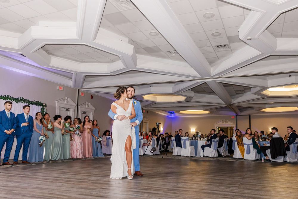 Couple sharing first dance at wedding reception with guests watching from tables.