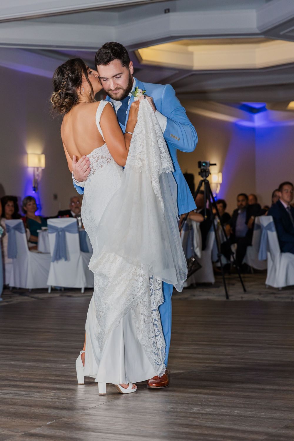 Wedding couple shares romantic first dance in a ballroom with elegant white and blue decor.