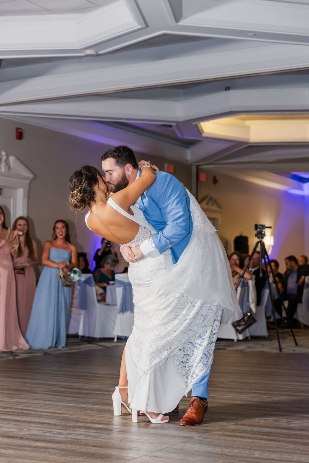 Newlyweds perform elegant dip during first dance at wedding reception with blue uplighting.