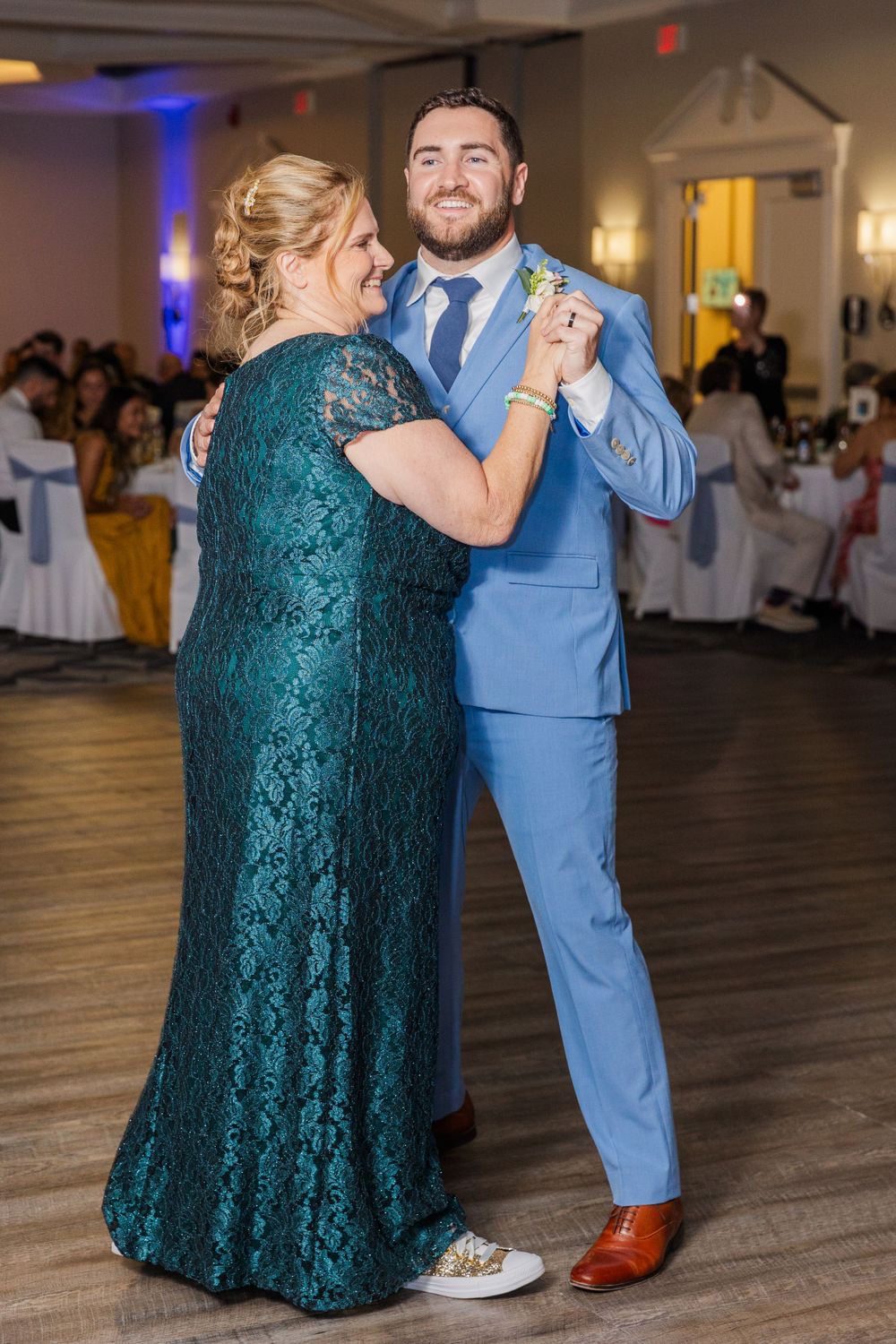Dancers in formal attire share special moment during wedding reception on wooden dance floor.
