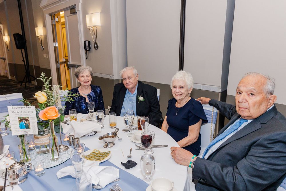 Guests seated at an elegantly decorated round table with blue tablecloths at a formal dinner event.