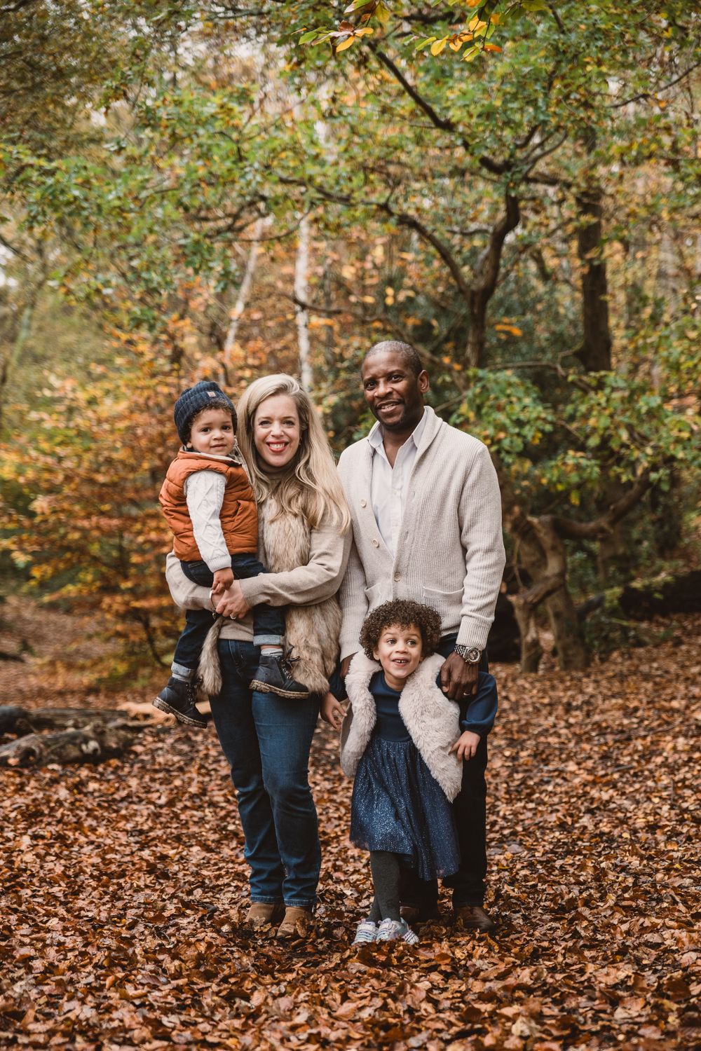 Family enjoys a playful autumn photography session together on fallen leaves in a forest setting.