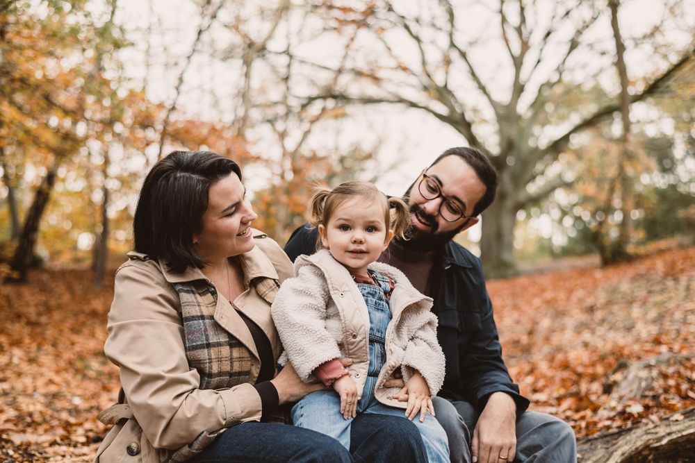 Family enjoying a tender moment together in a woodland during autumn with fallen leaves surrounding them.