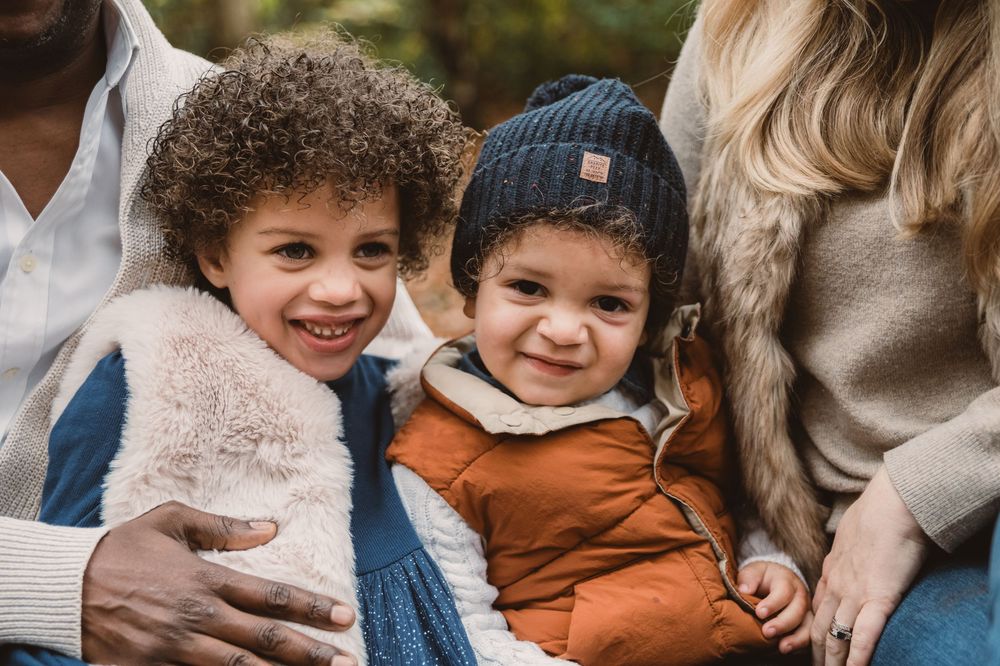 Happy family with children and infants laughing together outdoors during a photo session in autumn.