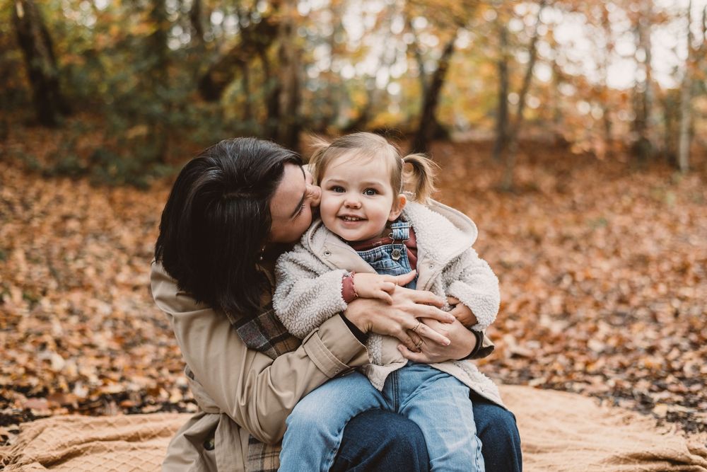 A loving family moment captured in autumn with fallen leaves scattered on the ground during a photo session.
