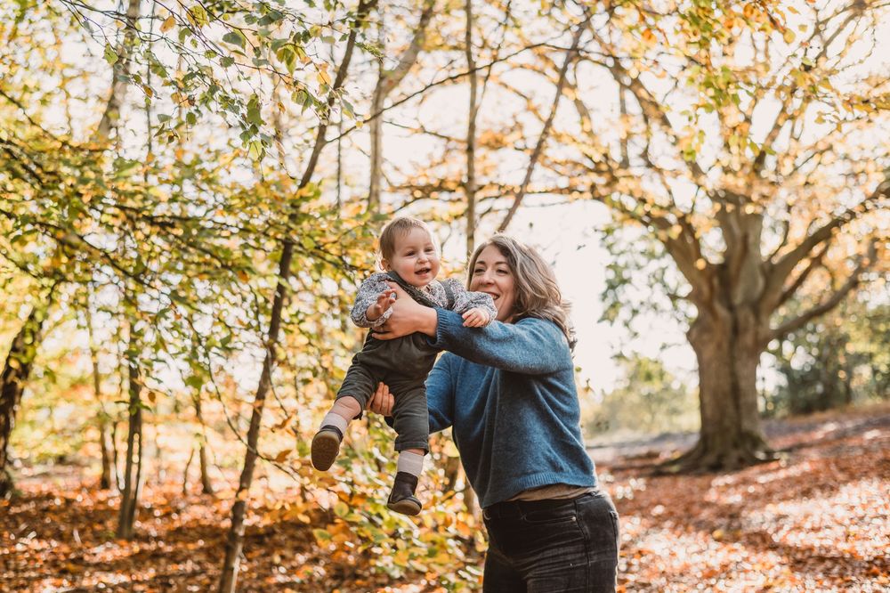 A mother and child play in autumn forest setting with golden sunlight filtering through the trees.