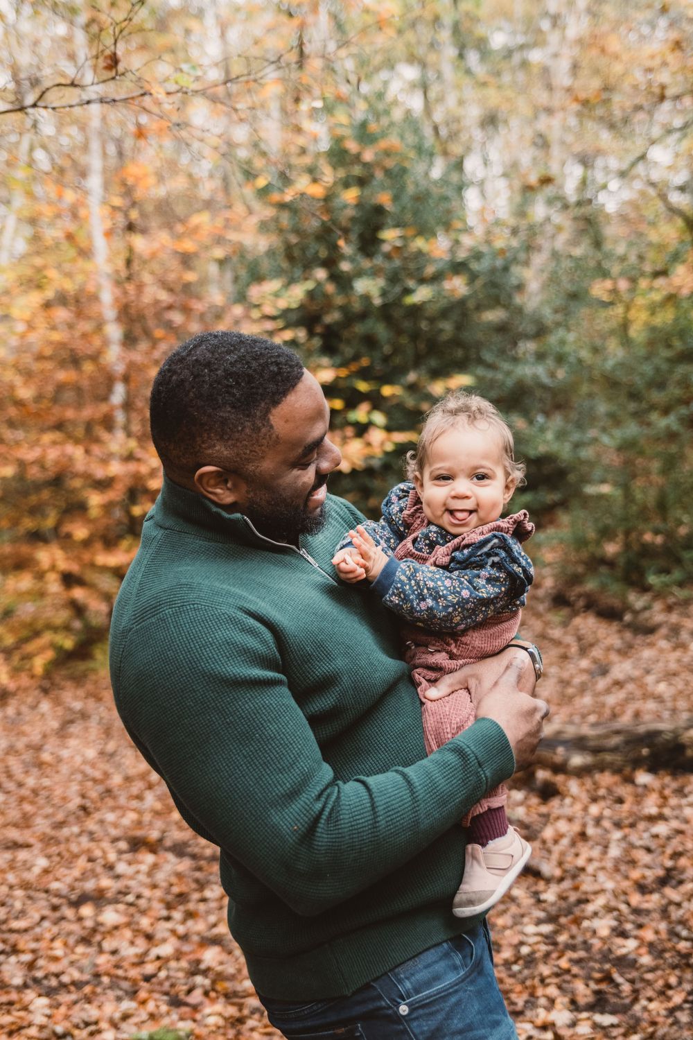 A tender autumn moment between parent and child captured in a wooded setting with golden fall foliage.
