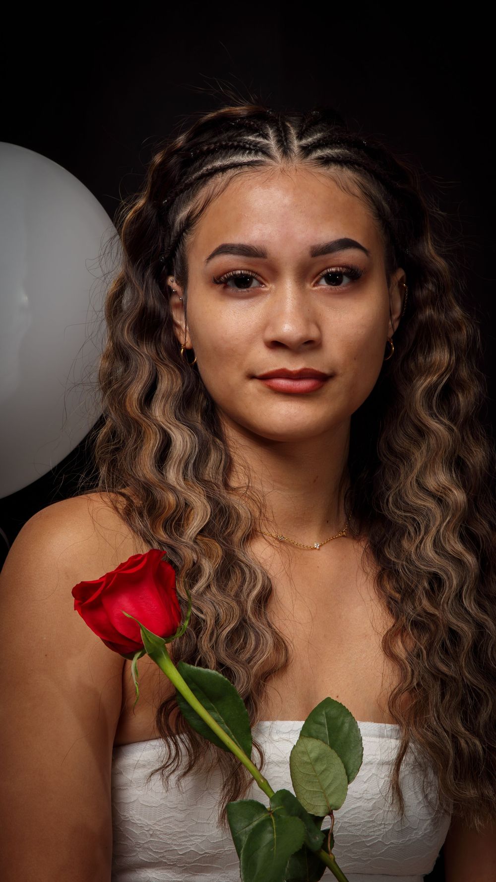 A beautiful girl holding red roses with white balloons in background