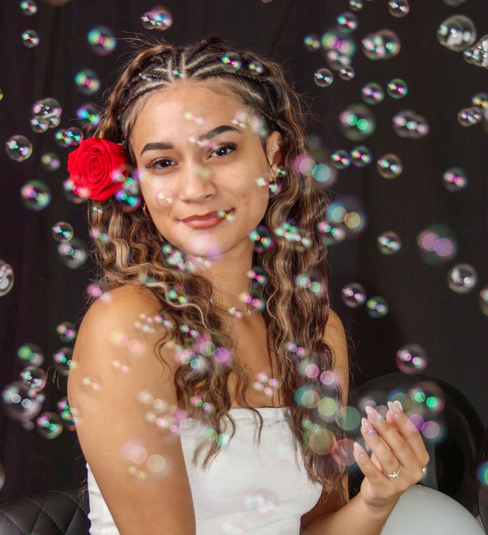A beautiful girl with a single red rose above her right ear,  with bubbles floating across her face