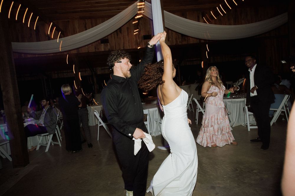 A wedding reception shows multiple guests dancing and having fun on a dimly lit dance floor.