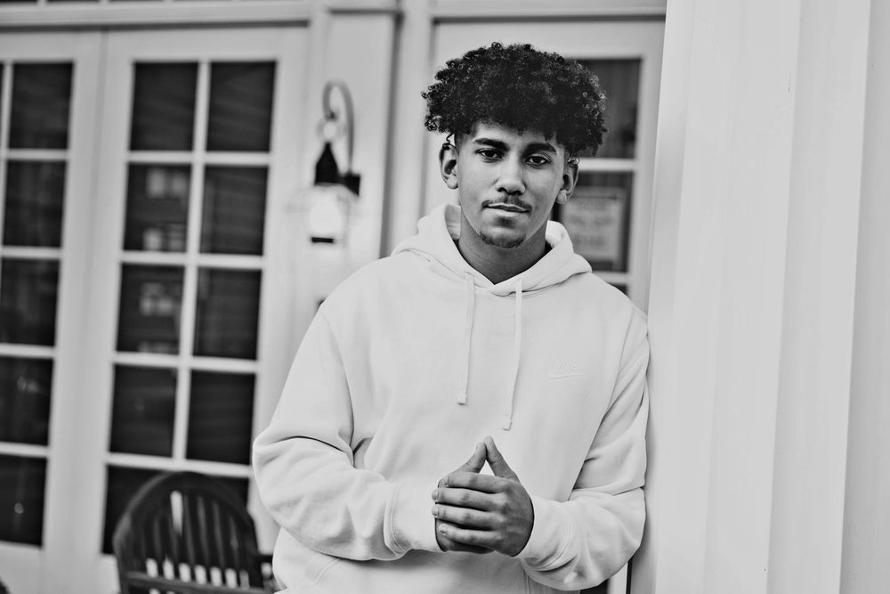Young man in white hoodie posing outdoors in black and white photo.