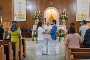 Catholic church sanctuary with wooden paneling and white-covered chairs for a ceremony.