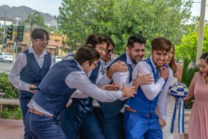 Wedding party embraces in a celebratory group hug on a sunny day.