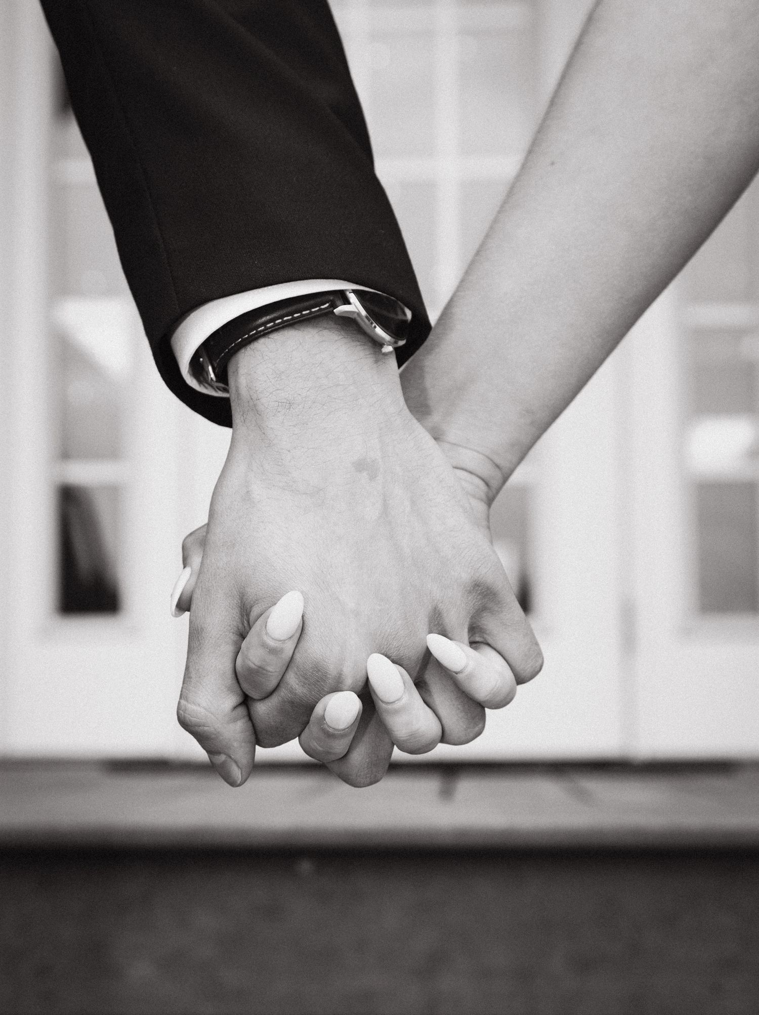 Black and white close-up photo of two people holding hands, with one person wearing a watch on their wrist.