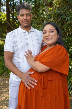Couple in white shirt and rust dress showing engagement ring in outdoor setting.