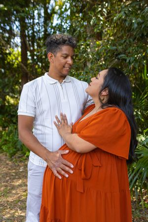 Happy couple embracing outdoors, wearing white shirt and rust-colored dress.