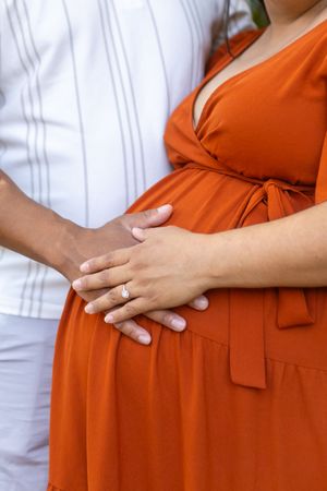 Hands gently cradling a pregnant belly in a vibrant orange maternity dress.
