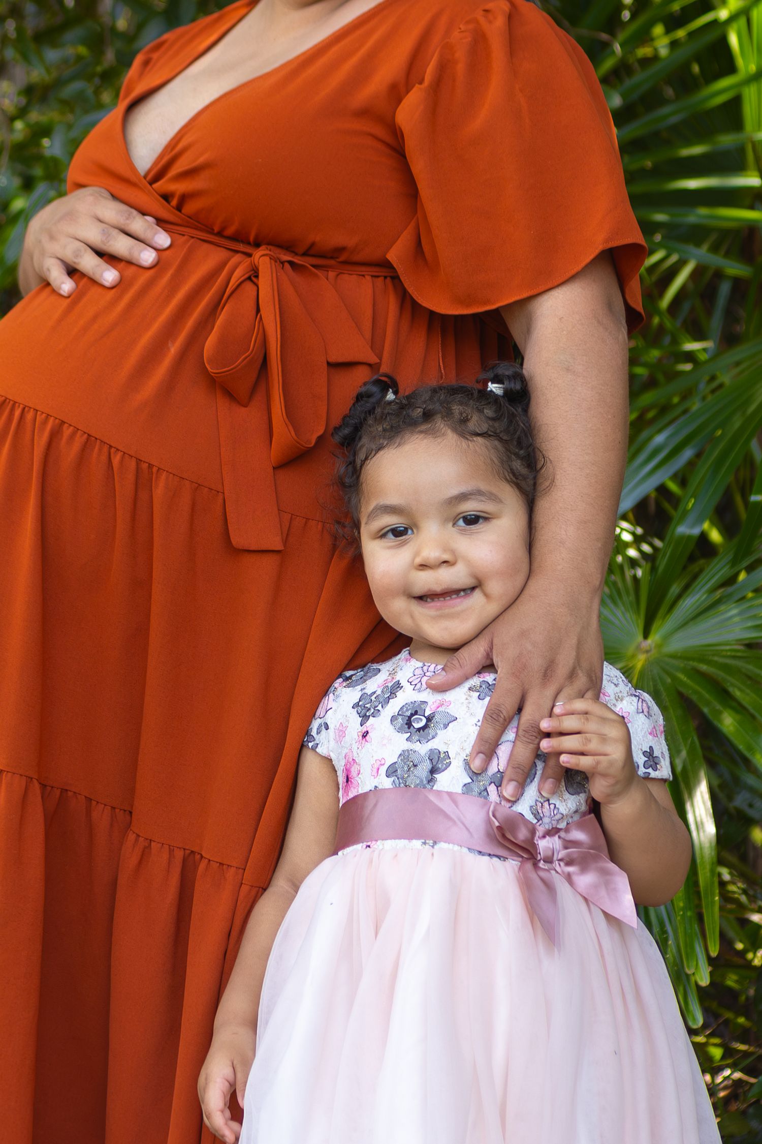 Close-up of maternity dress and pink floral children's dress against tropical greenery.
