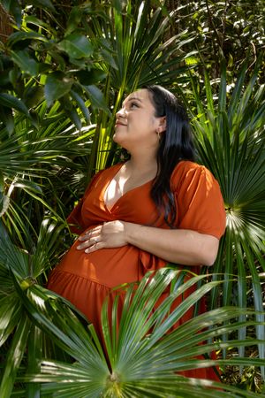 Natural maternity portrait with palm leaves creating dynamic composition.