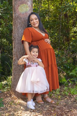 A touching family portrait in a wooded setting with matching rust and pink dresses.