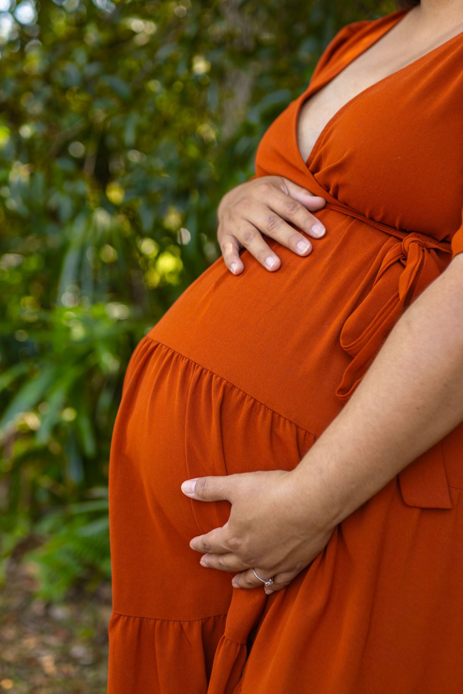 Side view of burnt orange maternity dress showing baby bump against garden background.