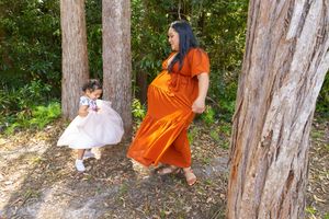 Whimsical forest photoshoot showing figures in orange and white dresses playing among tall trees.