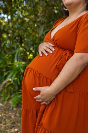 Close-up view of a rust-colored maternity dress against a natural outdoor background.