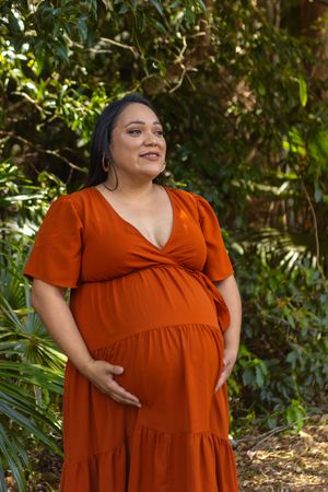 Woman wearing a rust-colored maxi dress poses confidently in a garden setting.