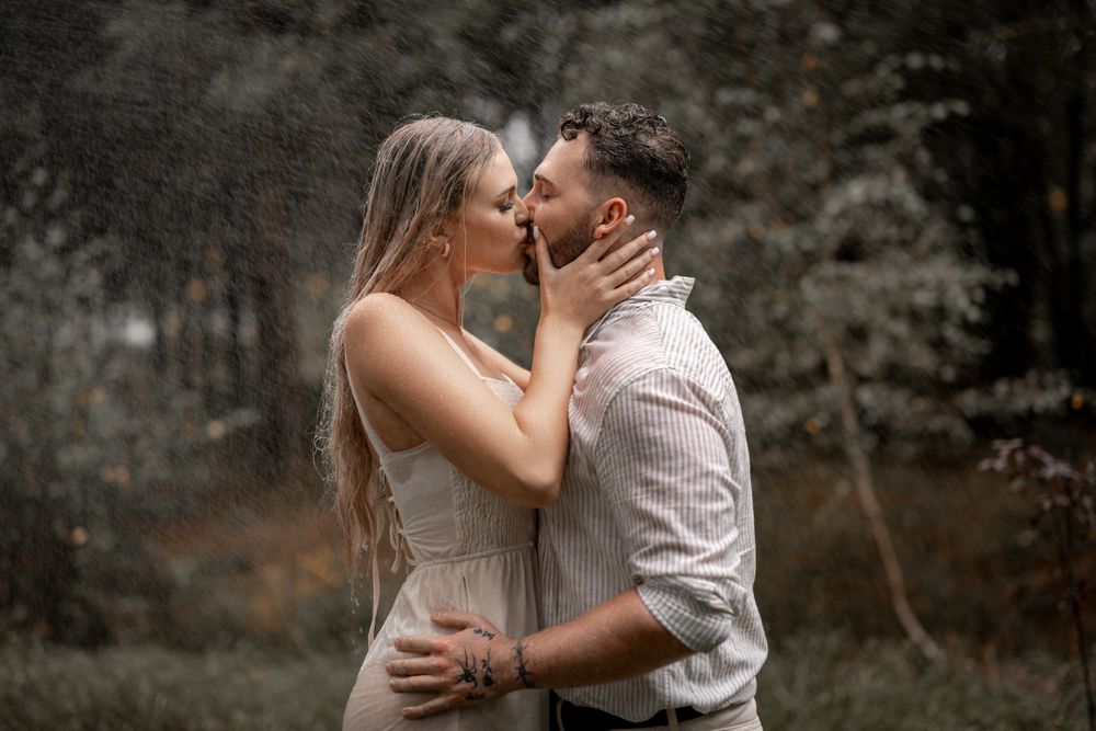 Intimate kiss captured in moody forest setting with dramatic lighting.