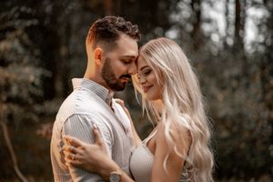 Romantic couple embrace in soft natural lighting with forest backdrop.