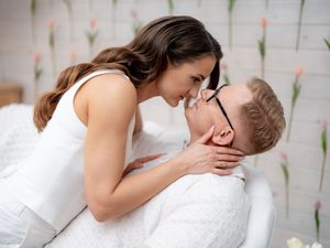 Two people dressed in white clothing sharing an intimate romantic moment against a light blurred background.