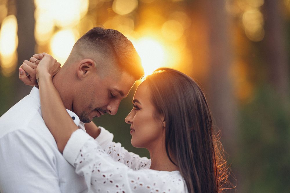 Intimate moment between couple backlit by golden sunset through trees.